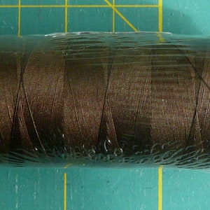 K&ouml;nnte beinhalten: Eine Spule braunen Fadens, verpackt in Plastik mit einem roten Etikett mit der Aufschrift "1285".