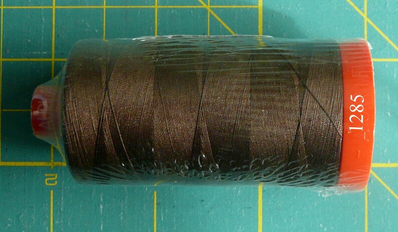 K&ouml;nnte beinhalten: Eine Spule braunen Fadens, verpackt in Plastik mit einem roten Etikett mit der Aufschrift "1285".
