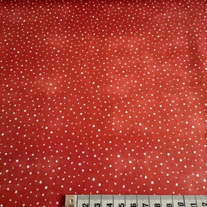 Könnte beinhalten: Roter Stoff mit weißem Punktmuster. Ein Maßband liegt auf dem Stoff und zeigt Maße in Zoll.