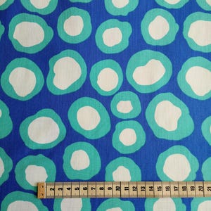 Könnte beinhalten: Blauer Stoff mit einem Muster aus weißen und türkisfarbenen Kreisen. Ein Holzliniall mit Zollmarkierungen liegt auf dem Stoff.