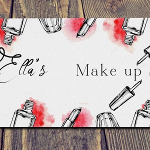 May include: White mouse mat with a watercolour background of pink and red splotches. The mouse mat has a black and white illustration of makeup brushes, lipstick, nail polish bottles, and the text "Ella's Make up Station".