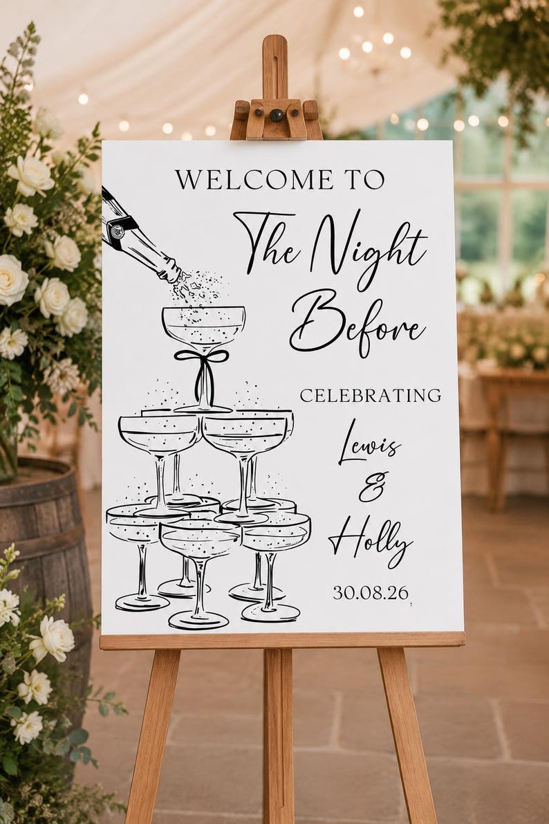 May include: A white rectangular sign on a wooden easel featuring black line art of a champagne bottle pouring into a stacked tower of coupe glasses. The text reads: WELCOME TO The Night Before CELEBRATING Lewis & Holly 30.08.26 in black font.