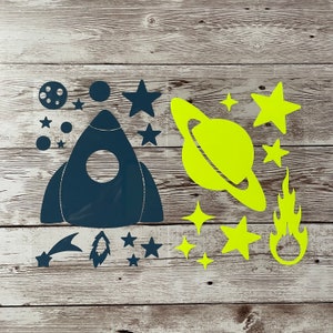 May include: A set of space-themed iron-on decals featuring a rocket ship, planets, stars, and a shooting star. The decals are in navy blue and neon yellow.
