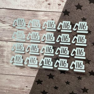 May include: Twenty-five white stickers with the number 116 printed on them. The stickers are arranged in five rows of five stickers each. The stickers are on a clear plastic sheet.