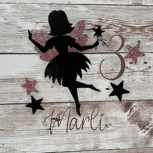 Könnte beinhalten: Eine schwarze Silhouette einer Fee mit rosa Glitzerflügeln, die einen Sternenstab hält. Die Fee ist umgeben von rosa Glitzersternen und der Zahl 3. Der Name "Marli" ist in Kursivschrift unter der Fee geschrieben.