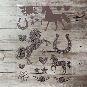 Pode incluir: Uma folha de vinil termocolante com uma variedade de designs com glitter e sem glitter, incluindo cavalos, ferraduras, corações, estrelas e flores. Os designs são em tons de rosa e marrom.