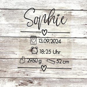 Könnte beinhalten: Ein weißes Holzschild mit schwarzem Text und Symbolen, das die Geburt von Sophie ankündigt. Das Schild enthält das Geburtsdatum und die Uhrzeit, das Gewicht und die Länge. Der Text lautet: "Sophie -♡- 13.09.2024 18:25 Uhr 2960 g -♡- 52 cm"