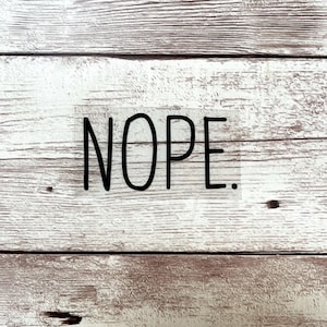 Puede incluir: Un fondo de madera blanco con la palabra "NOPE." escrita en negro.