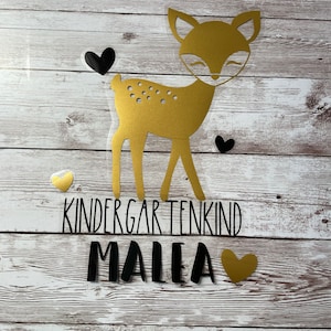 Könnte beinhalten: Goldene Glitzer-Hirsch-Silhouette mit schwarzen Herzen und dem Text "Kindergartenkind Malea" in Schwarz.