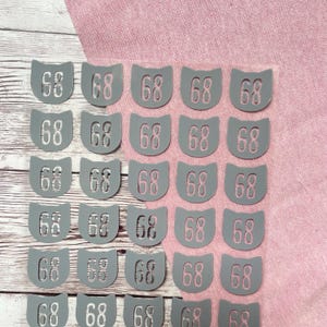 May include: Twenty-five grey fabric labels with the number "68" printed on each. The labels are arranged in five rows of five.