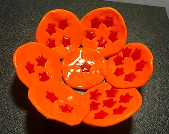 May include: Orange ceramic bowl with red star-shaped details. The bowl is shaped like a flower with seven petals.