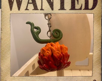 May include: A red, orange, and green clay charm shaped like a flame with a metal chain attached. The charm is labeled "SMERA MERA DEVIL FRUIT".
