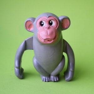 May include: A gray plastic toy monkey with pink ears and a pink face. The monkey has large, round eyes and a wide smile.