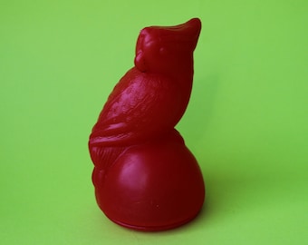 May include: A red plastic bird figurine with a round base. The bird is perched on the base with its head turned to the side.