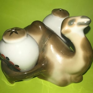 May include: A ceramic camel salt and pepper shaker set. The camel is brown and white with gold accents. The salt and pepper shakers are white with floral designs.