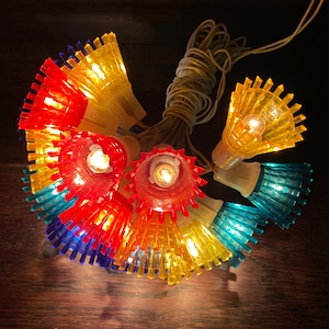 May include: A string of colorful, vintage Christmas lights with a fan-shaped design. The lights are red, yellow, and blue and have a warm white glow.