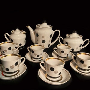May include: A white porcelain tea set with black polka dots and gold accents. The set includes a teapot, creamer, sugar bowl, and six teacups and saucers.