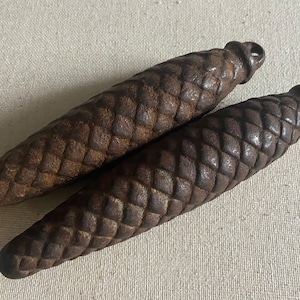 May include: Two antique cast iron pine cone shaped door pulls. The pulls are a dark brown colour and have a textured surface.