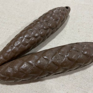 May include: Two brown, textured, ceramic pine cone ornaments. The pine cones are detailed with a rough, textured surface.