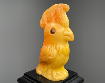 May include: A yellow ceramic bird figurine with a detailed design and a brown eye. The bird is standing on a black base.