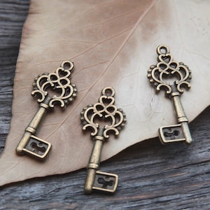 Könnte beinhalten: Drei verzierte Schlüsselanhänger im antiken Stil aus Metall mit bronzefarbener Oberfläche. Die Schlüssel haben komplizierte Designs und sind perfekt, um Schmuck oder Bastelarbeiten einen Vintage-Touch zu verleihen.