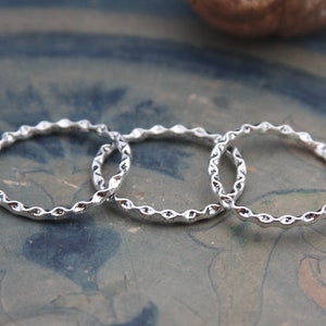 Könnte beinhalten: Drei silberne Ringe mit einem strukturierten, wellenförmigen Design. Die Ringe sind übereinander gestapelt.