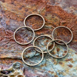 Könnte beinhalten: Fünf goldfarbene Metallringe in verschiedenen Größen sind in einem Kreis auf einer rostigen, braunen und grauen strukturierten Oberfläche angeordnet.
