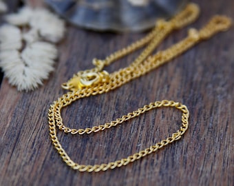 May include: A gold chain necklace on a wooden surface. The chain is made of small, linked circles.