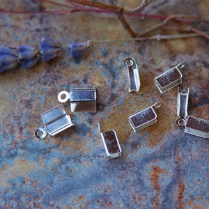 Op de afbeelding: Acht zilverkleurige metalen sluitingen voor het maken van sieraden. De sluitingen zijn rechthoekig met een kleine lus aan één uiteinde.
