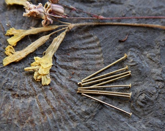 May include: A close-up of a group of eight gold-colored head pins on a dark gray textured surface. The pins are arranged in a fan shape.