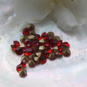 Könnte beinhalten: Nahaufnahme eines kleinen Haufens roter und goldener Strasssteine auf einer weißen, schillernden Oberfläche. Die Strasssteine sind in einem lockeren, organischen Muster angeordnet.