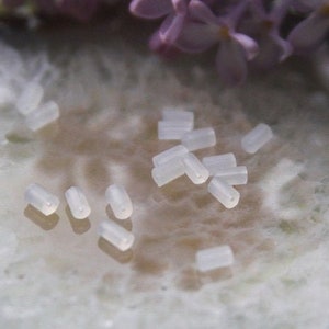 Könnte beinhalten: Nahaufnahme einer Gruppe kleiner, transparenter Plastikröhrchen, die auf einer weißen, strukturierten Oberfläche verstreut sind. Die Röhrchen sind etwa 1,2 cm lang und 0,3 cm im Durchmesser.