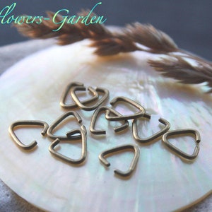 Könnte beinhalten: Nahaufnahme eines Stapels kleiner, goldfarbener Dreiecks-Sprünge auf einer weißen, schillernden Oberfläche. Die Sprungringe sind etwa 1,25 cm groß.