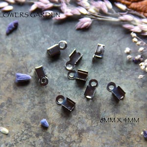Op de afbeelding: Zilveren metalen sluitingen, 8 mm x 4 mm, voor het maken van sieraden. De sluitingen zijn verspreid over een getextureerd oppervlak met gedroogde bloemen.