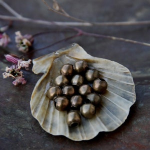 May include: A collection of round, metallic beads in a shell-shaped dish. The beads are a mix of gold and bronze tones.