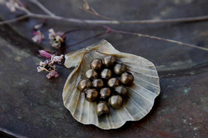 May include: A collection of round, metallic beads in a shell-shaped dish. The beads are a mix of gold and bronze tones.