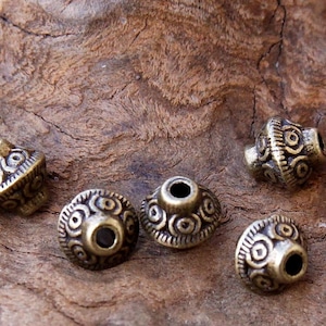 Könnte beinhalten: Sechs antike goldfarbene Metallperlen mit einem dekorativen, kreisförmigen Muster. Die Perlen haben ein Loch in der Mitte zum Aufziehen.