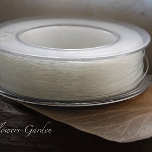 Könnte beinhalten: Eine Spule weißen Fadens auf einer durchsichtigen Plastikspule. Die Spule liegt auf einem braunen Blatt.