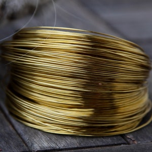 Könnte beinhalten: Nahaufnahme einer Spule mit goldfarbenem Draht. Der Draht ist fest um die Spule gewickelt und bildet eine glatte, gleichmäßige Oberfläche.