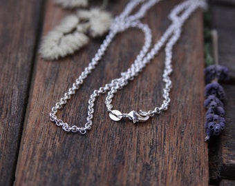 May include: A silver chain necklace with a lobster clasp closure. The chain is on a wooden surface.