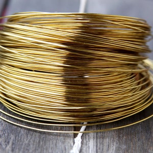 Könnte beinhalten: Eine durchgehende Spule aus dünnem, goldfarbenem Metalldraht, der zu einer dichten, zylindrischen Form aufgewickelt ist. Der Draht hat eine glatte, reflektierende Oberfläche und ist in mehreren überlappenden kreisförmigen Schichten angeordnet, was ein gleichmäßiges, glänzendes Aussehen erzeugt.
