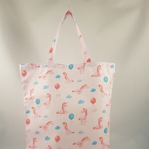 Könnte beinhalten: Eine rosa Canvas-Tragetasche mit einem sich wiederholenden Muster aus rosa Einhörnern und blauen und roten Ballons. Die Einhörner sind alle in die gleiche Richtung ausgerichtet und haben ein weißes Horn und eine rosa Mähne.
