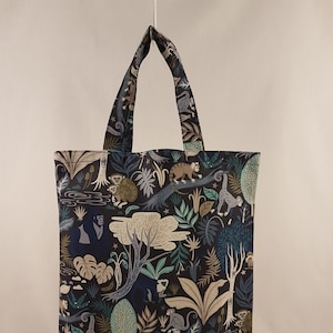 Op de afbeelding: Een draagtas met een donkerblauw junglepatroon met apen, bomen en bladeren in groen, beige en grijs. De tas heeft bijpassende handvatten en een rechthoekige vorm.