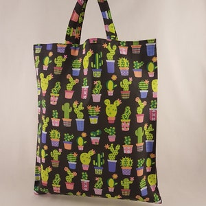 Op de afbeelding: Een zwarte draagtas met een herhaald patroon van cactussen in kleurrijke potten. De cactussen zijn groen en geel, de potten blauw, paars en oranje. De tas heeft een bijpassende handgreep en is gemaakt van stevige stof.