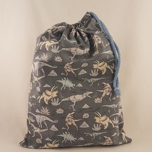 Könnte beinhalten: Eine graue Kordeltasche mit einem Dinosaurier-Druck. Die Dinosaurier sind in Schattierungen von Hellblau, Gelb und Weiß. Die Tasche hat eine hellblaue Kordel.