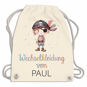 May include: A cream-colored drawstring backpack featuring a cartoon pirate illustration. The pirate has an eye patch, a hat with a skull, and colorful feathers. The text "Wechselkleidung von PAUL" is written in a rainbow font.