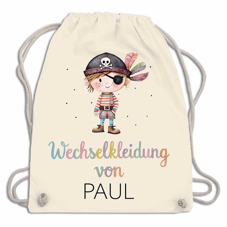 May include: A cream-colored drawstring backpack featuring a cartoon pirate illustration. The pirate has an eye patch, a hat with a skull, and colorful feathers. The text "Wechselkleidung von PAUL" is written in a rainbow font.