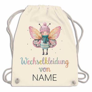 May include: A cream-colored drawstring backpack featuring a whimsical butterfly design. The butterfly is depicted with pink and yellow wings, a blue scarf, and a pink hat. The text "Wechselkleidung von NAME" is printed on the bag.