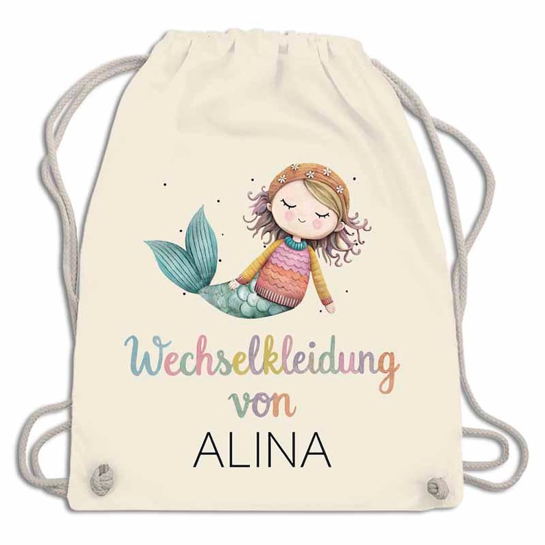 May include: A cream-colored drawstring backpack featuring a watercolor illustration of a mermaid with a teal tail and a sweater. The text "Wechselkleidung von ALINA" is written in colorful letters.