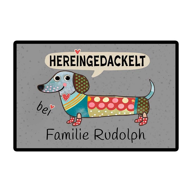 May include: A decorative doormat featuring a cartoon dachshund with a colorful patchwork design. The dog has a speech bubble with the German text "HEREINGEDACKELT" and the words "Familie Rudolph" below.